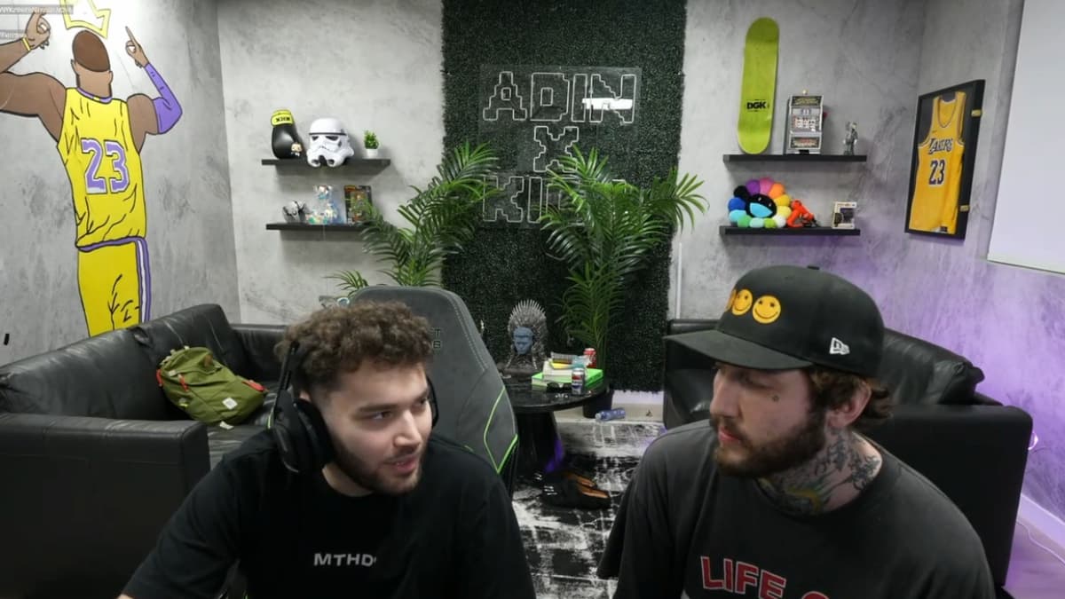 Adin Ross and Faze Banks speaking to each other in a small room with plants and pink accents.