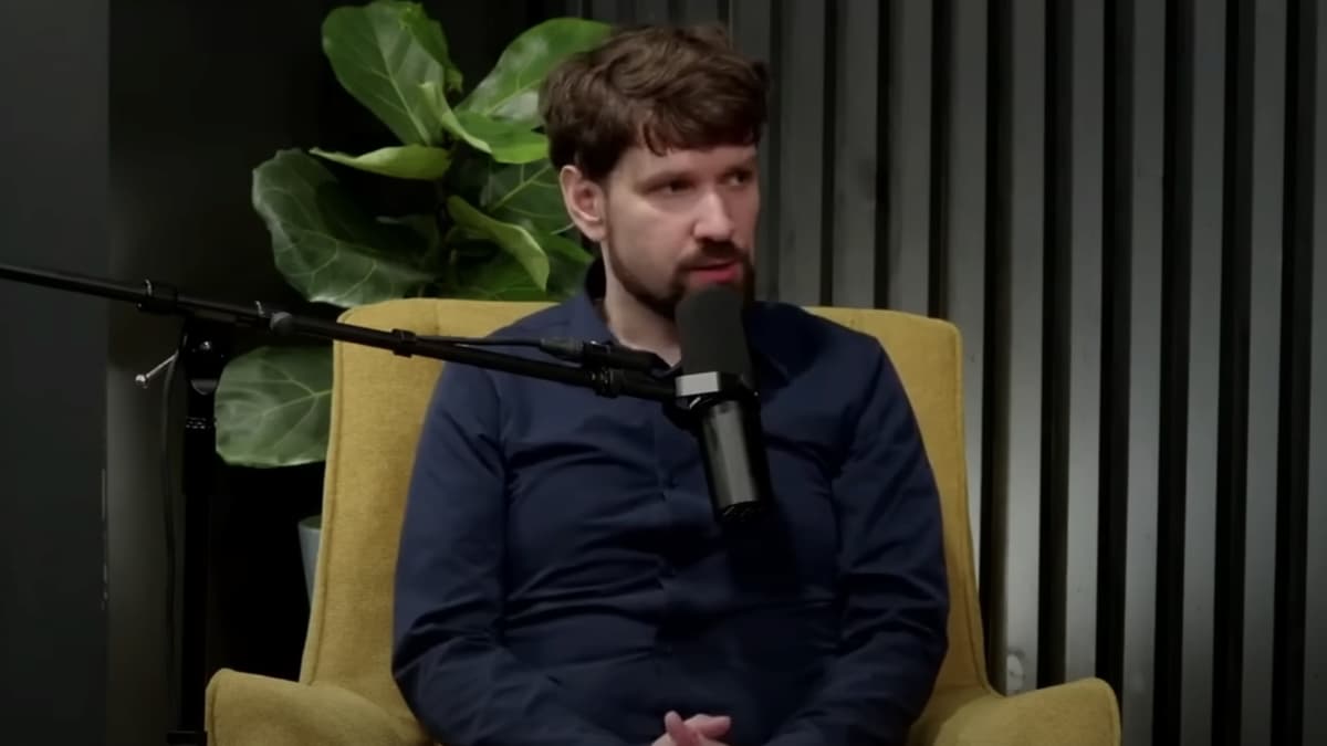 Streamer Destiny sitting in a chair with his arms crossed with a big plant behind him.