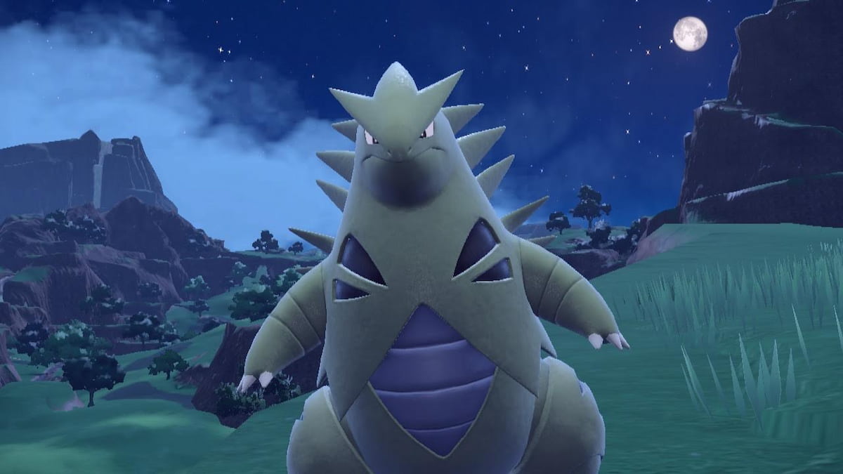 Tyranitar standing in a grassy field at night in Pokémon Scarlet and Violet.