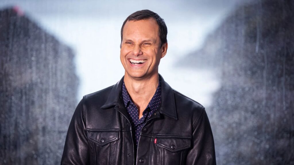 John Needham, Riot Games' President of Publishing & Esports, smiling and wearing a black leather jacket.