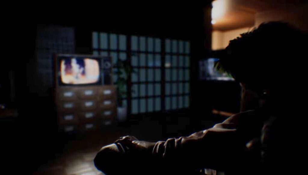 Dark shot of Mr. Kim sitting on the couch, watching the news