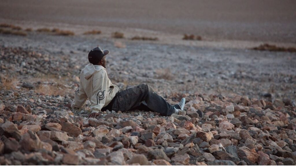 Kai Cenat sitting on the beach while reflecting
